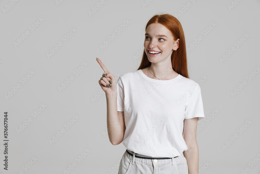 Image of happy ginger girl smiling and pointing finger aside Image of happy ginger girl smiling and pointing finger aside