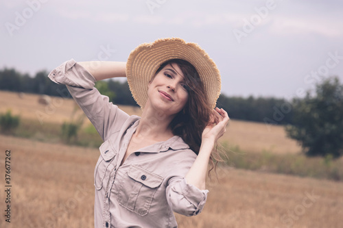 A young attractive girl in a straw hat stands in a field.