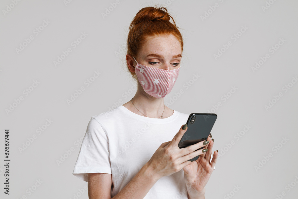 Fototapeta premium Image of focused ginger girl in face mask using mobile phone