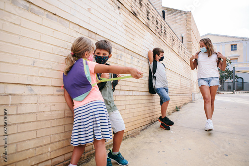 Caucasian children of different ages with protective masks and backpacks talking outside school. First day of school after the coronavirus pandemic. New rules for the Covid-19 new normal.