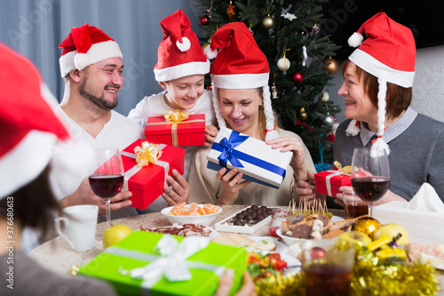 Big friendly family celebrating Christmas with gifts against backdrop of decorated fir tree