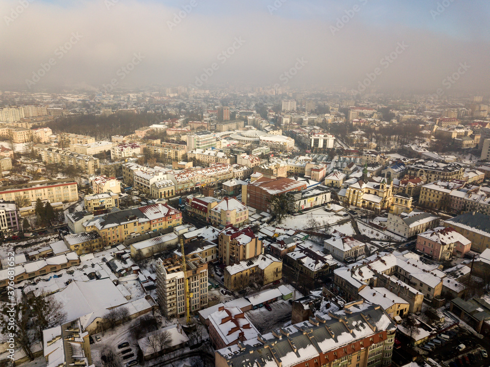 Fototapeta premium Aerial black and white winter top view of modern city center with tall buildings and parked cars on snowy streets.