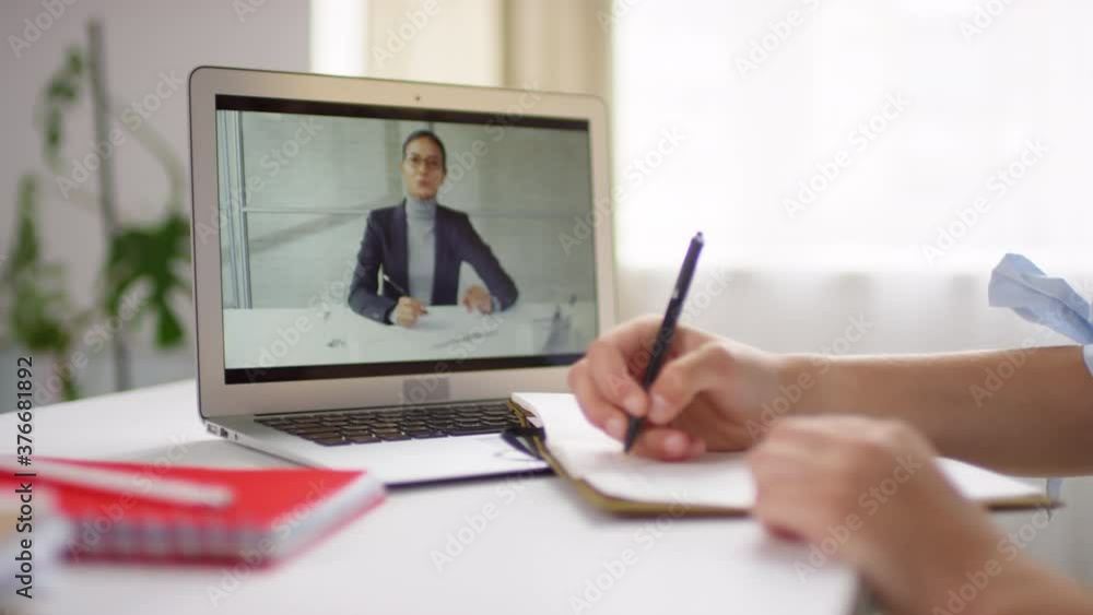Mid-section of hands of unrecognizable schoolgirl learning remotely. She is writing in her notebook while video calling female teacher Mid-section of hands of unrecognizable schoolgirl learning remotely. She is writing in her notebook while video calling female teacher