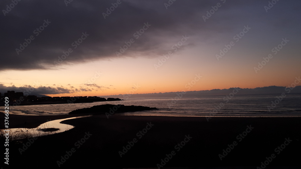 Fototapeta premium Atardecer en las costas gallegas desde el pueblo de San Cosme De Barreiros. se aprecian las ultimas luces sobre la arena, el agua y el arroyo que desemboca en el mar