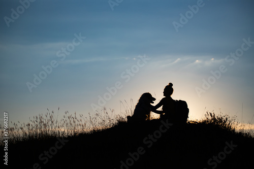 Woman with her dog sitting on the hill in the sunset.