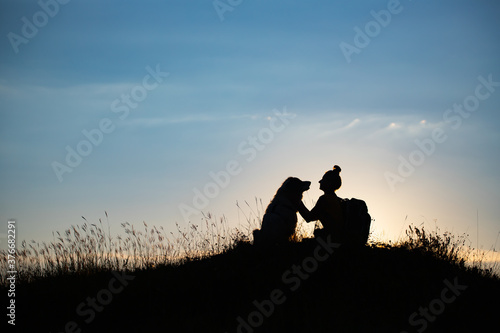 Woman with her dog sitting on the hill in the sunset. © erika8213