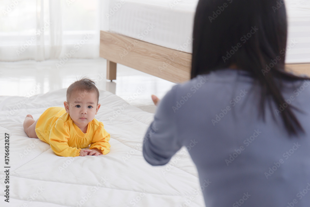 An Asian infant who is practicing crawling With her mother sitting on the other side of her soft white cloth in the bedroom An Asian infant who is practicing crawling With her mother sitting on the other side of her soft white cloth in the bedroom
