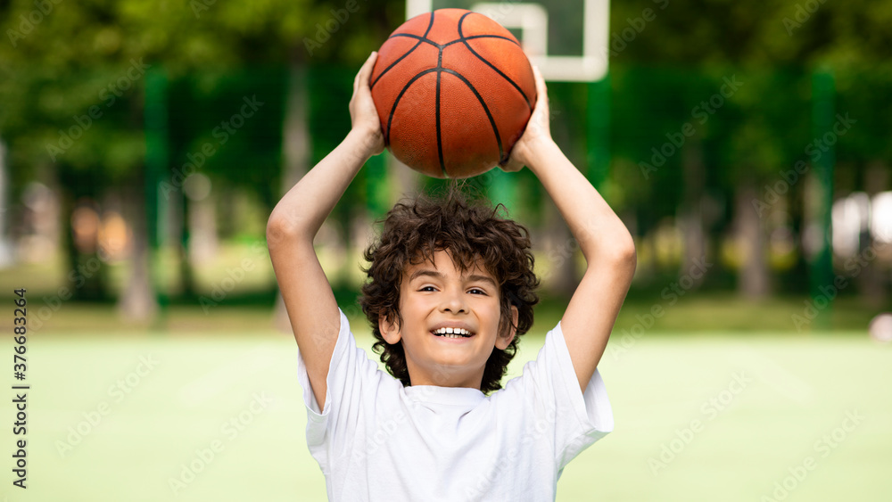 Portrait of sportive curly boy throwing basket ball