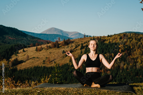 A young woman is practicing yoga at mountains. Relaxing in nature. Young girl doing yoga fitness exercise outdoor in the beautiful landscape. Morning sunrise, Namaste Lotus pose. Meditation.