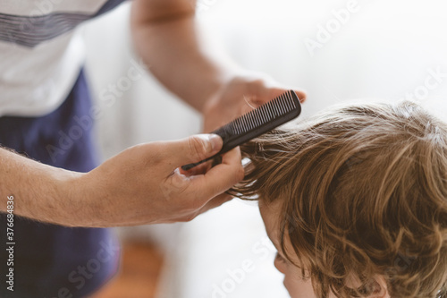 Father cuts her son hair in the room. Family during quarantine, Scissors and a comb in male hands