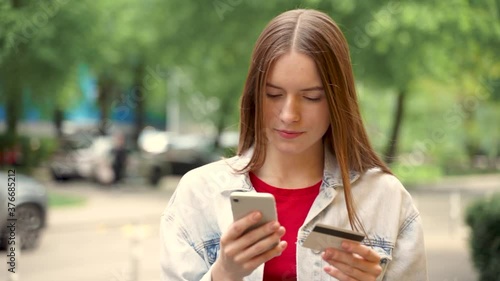 Pretty young woman shopping online with her smartphone and paying with credit card outdoors