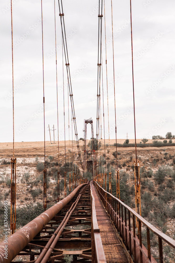 Obraz premium Old iron non-functioning suspension bridge over a dried river side view. Old pedestrian bridge in Moldova. 