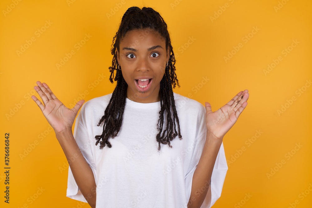 Optimistic Young dark skinned woman with braids hair wearing white t-shirt raises palms from joy, happy to receive awesome present from someone, shouts loudly, Excited caucasian male screaming. Optimistic Young dark skinned woman with braids hair wearing white t-shirt raises palms from joy, happy to receive awesome present from someone, shouts loudly, Excited caucasian male screaming.