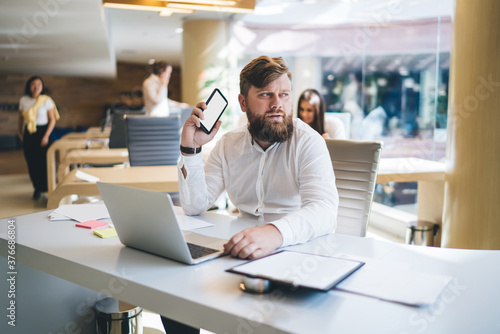 Contemplating businessman using smartphone in modern office