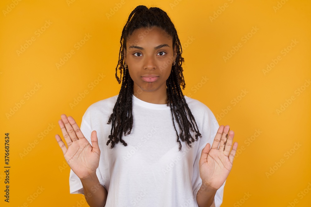 Φωτογραφία Serious Young dark skinned woman with braids hair wearing white t-shirt over yel
