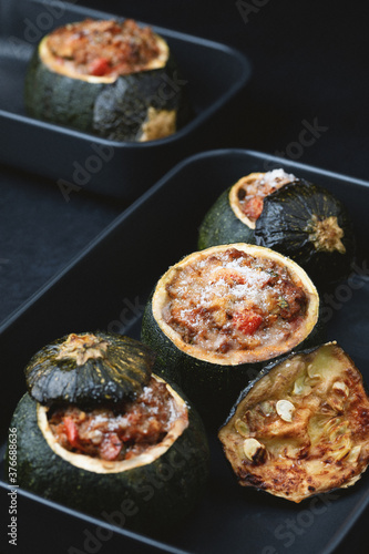 Round zucchini stuffed with meat, tomatoes and parmesan on dark plates. Dark background.