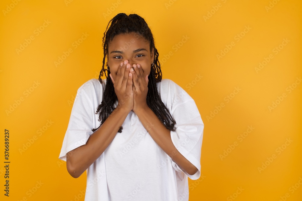 Vivacious Young dark skinned woman with braids hair wearing casual clothes trendy , giggles joyfully, covers mouth, has fun alone, has natural laughter, hears positive story or funny anecdote Vivacious Young dark skinned woman with braids hair wearing casual clothes trendy , giggles joyfully, covers mouth, has fun alone, has natural laughter, hears positive story or funny anecdote