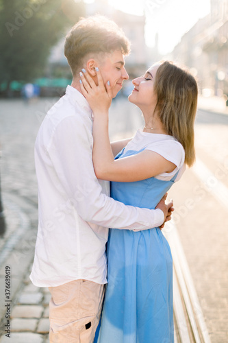 Lovely couple, boyfriendin white shirt and girlfriend in blue dress, looking at each other, smiling and hugging in old beautiful city in Europe. Couple, people, outdoor portrait concept