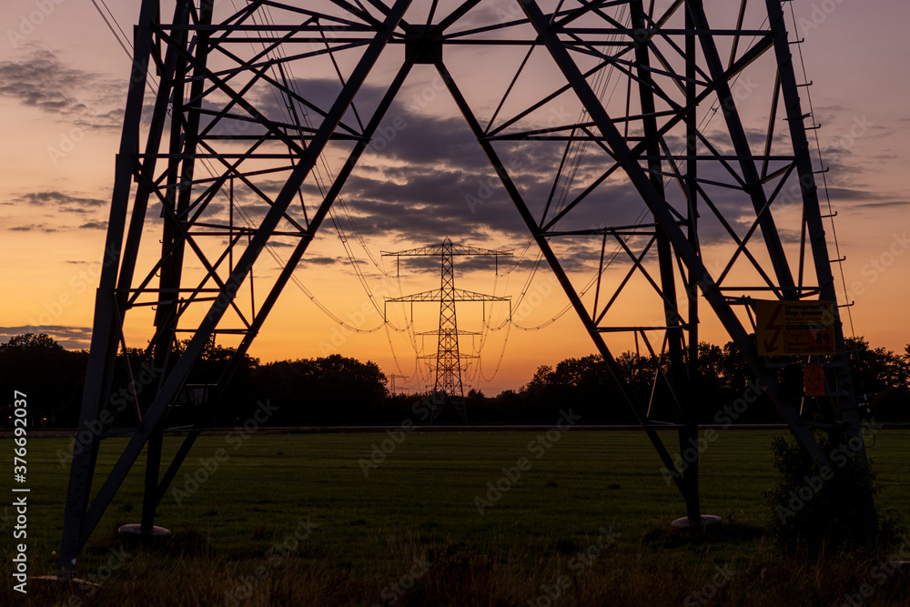 Sharp silhouette of part of an electricity tower construction and power lines against a colourful orange sunset sky with clouds