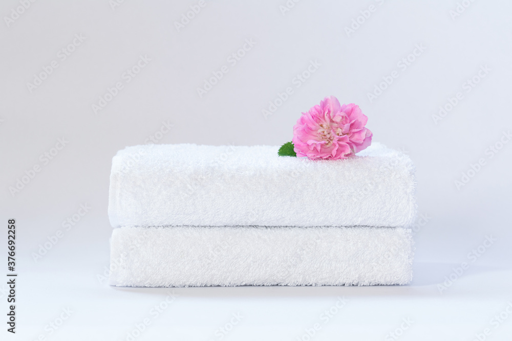 Two white neatly folded terry towels with a rose flower on a light background. Two white neatly folded terry towels with a rose flower on a light background.