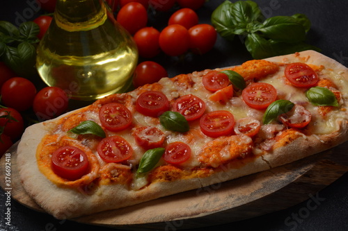 Flatbread pizza garnished with fresh cherry tomatoes,basil,cheese and olive oil on wooden pizza board. Dark background