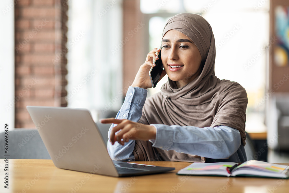 Arab woman in headscarf having conversation on phone at cafe Arab woman in headscarf having conversation on phone at cafe