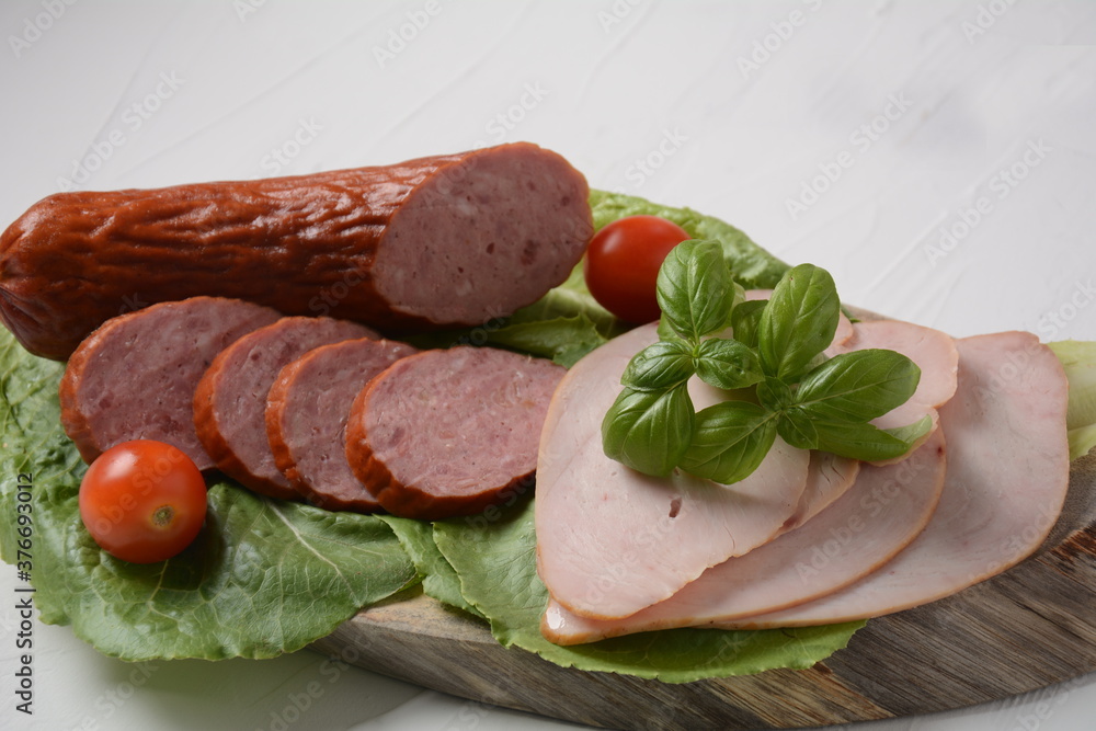 Sliced spicy smoked beef/ pork sausage and turkey pastrami slices. With lettuce leaf and basil,cherry tomatoes.