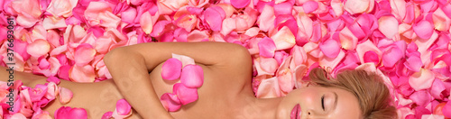 Beautiful slim young woman lying on petals of pink roses. Perfect figure.