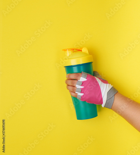 female hand holding plastic blue shaker bottle with a yellow cap