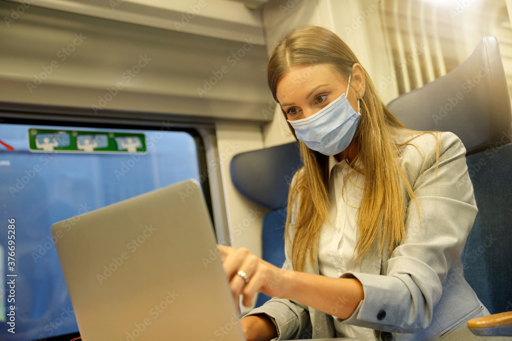 Businesswoman commuting by train, working on laptop and wearing face mask Businesswoman commuting by train, working on laptop and wearing face mask