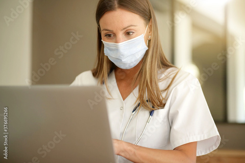 Portrait of nurse with face mask working on laptop in the office