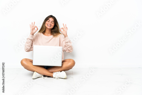 Young woman with a laptop sitting on the floor isolated on white background in zen pose © luismolinero