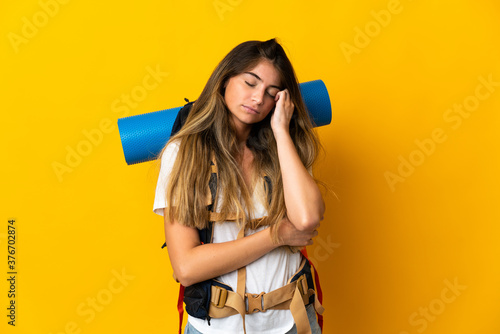 Young mountaineer woman with a big backpack isolated on yellow background with headache