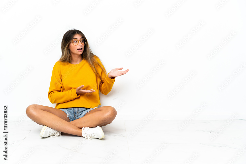 Young woman sitting on the floor isolated on white background with surprise facial expression Young woman sitting on the floor isolated on white background with surprise facial expression