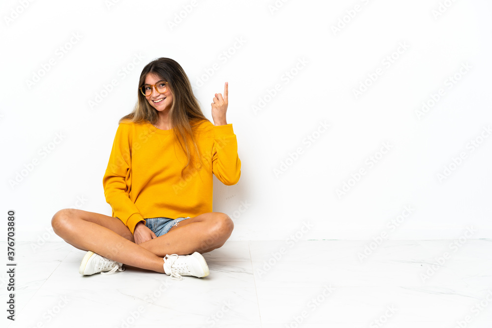 Young woman sitting on the floor isolated on white background showing and lifting a finger in sign of the best Young woman sitting on the floor isolated on white background showing and lifting a finger in sign of the best