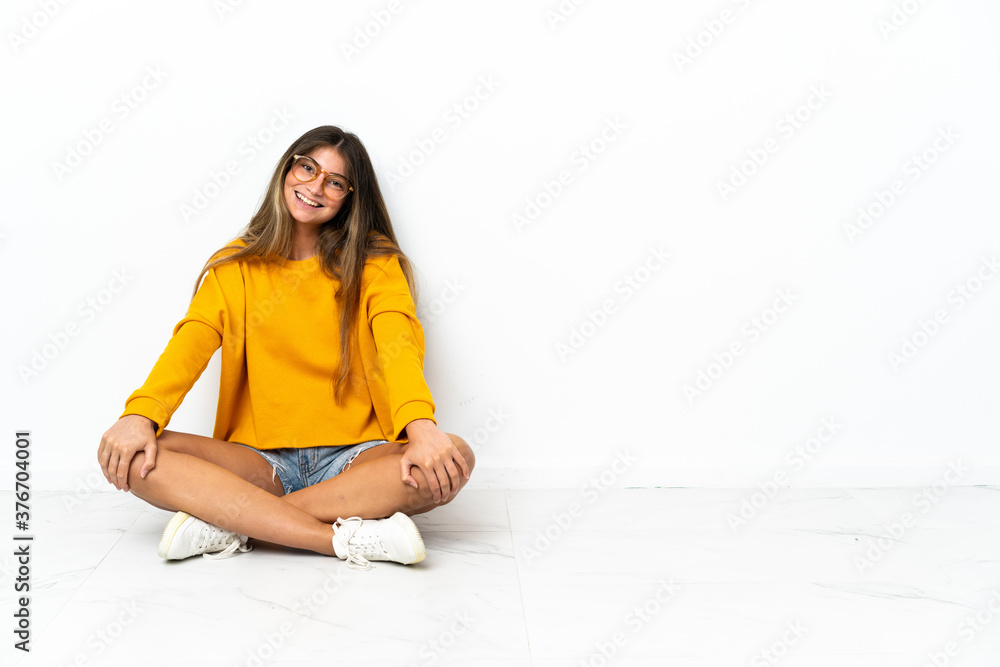 Young woman sitting on the floor isolated on white background with arms crossed and looking forward Young woman sitting on the floor isolated on white background with arms crossed and looking forward