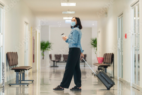 Wallpaper Mural Traveling young asian woman wearing face mask to protect covid19 virus and holding cup of coffee in her hand walking with suitcase bag at airport. Torontodigital.ca
