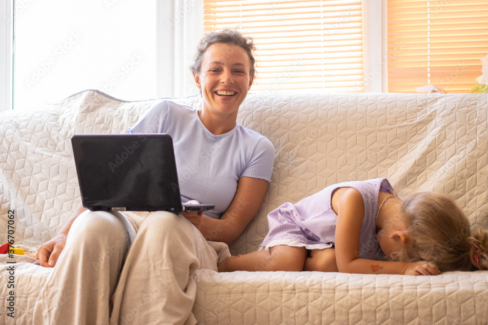 Happy smiling young mother and funny kid girl daughter having fun, watching cartoons on laptop, playing online games, sitting on sofa at home. Fooling around and laughing, spending time together Happy smiling young mother and funny kid girl daughter having fun, watching cartoons on laptop, playing online games, sitting on sofa at home. Fooling around and laughing, spending time together