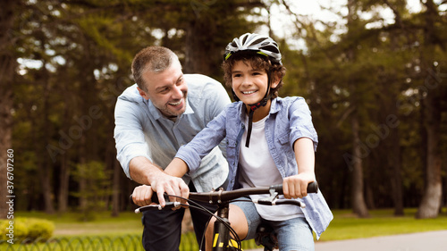 Boy learning to ride bicycle with his happy dad