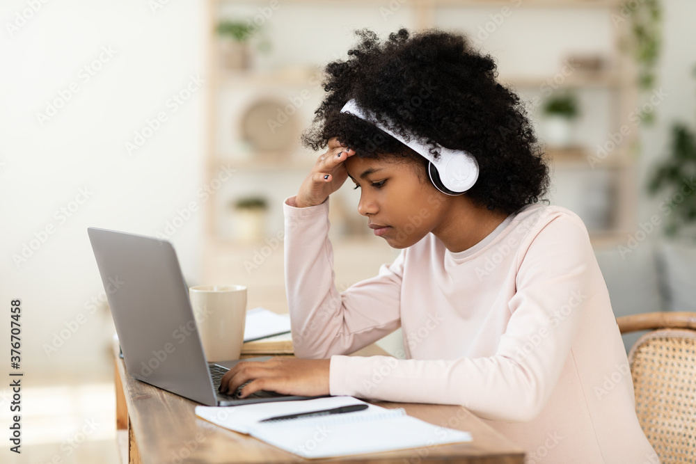 Girl At Laptop Doing Homework Online At Home, Wearing Earphones Girl At Laptop Doing Homework Online At Home, Wearing Earphones