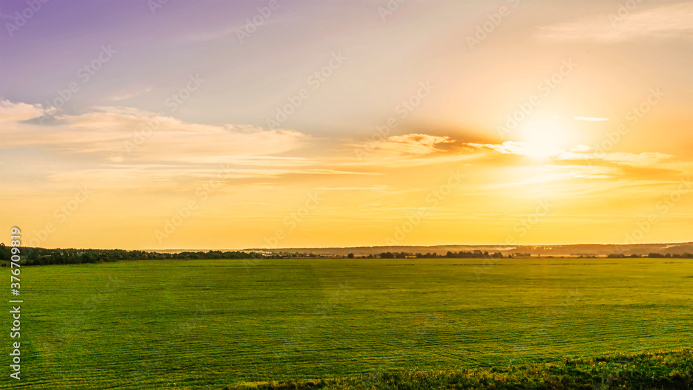 Scenic view at picturesque sunset in a green shiny field with bright cloudy sky , golden sun rays and glow on the background, summer valley landscape