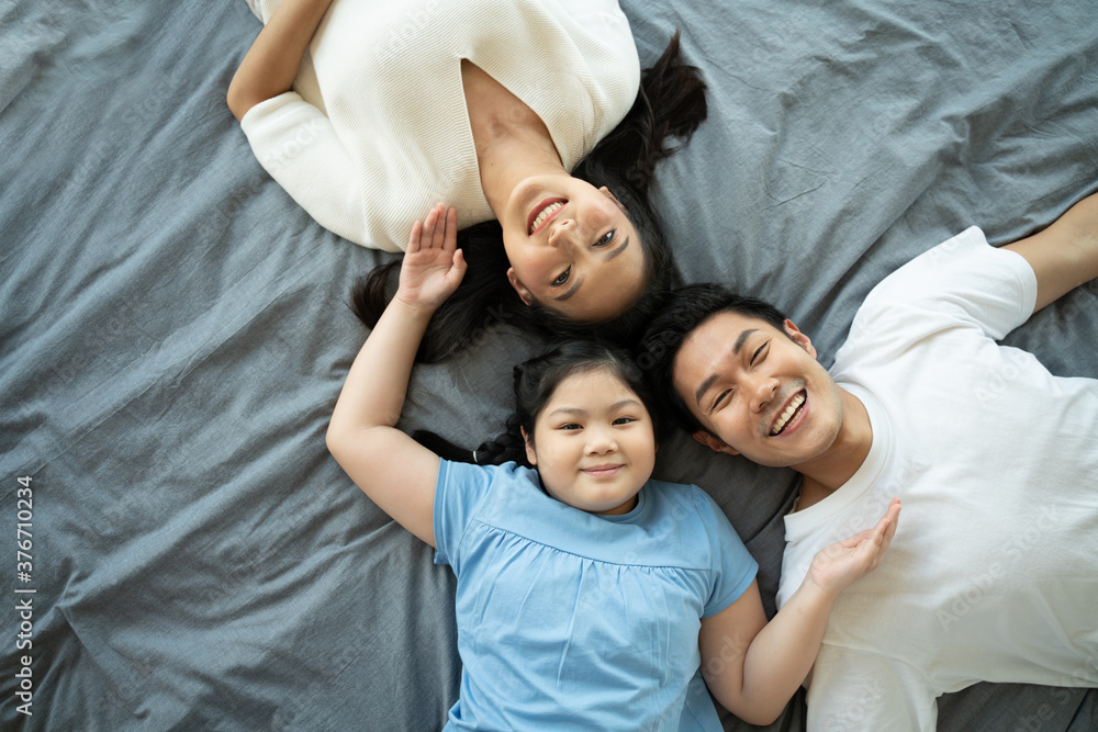 Top view of happy asian family laying on bed in the bedroom.Parents and daughter happy and smile in holiday.Family enjoying being together concept.