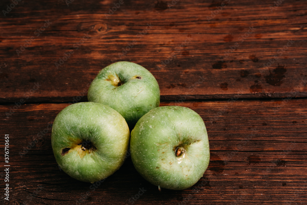 Fresh apples, autumn harvest. Three green apples are lying on a wooden table. Fresh apples on a wood textured brown background, mahogany material. Fresh apples, autumn harvest. Three green apples are lying on a wooden table. Fresh apples on a wood textured brown background, mahogany material.