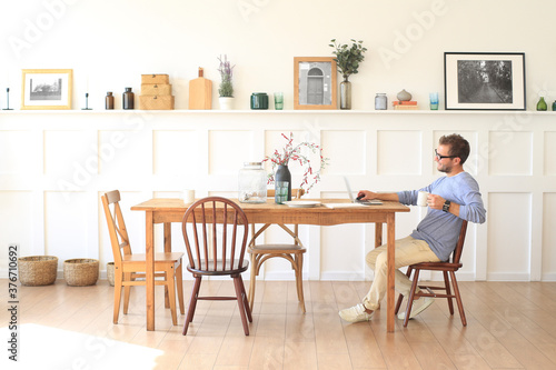 Young man with a cup of coffee works at the table at home in the morning