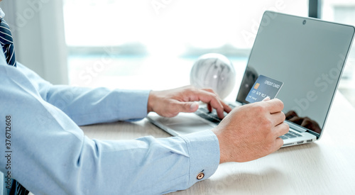 Fototapeta Naklejka Na Ścianę i Meble -  Businessman hand holding credit card to online shopping from home with laptop, payment e-commerce, internet banking, spending money for next holidays