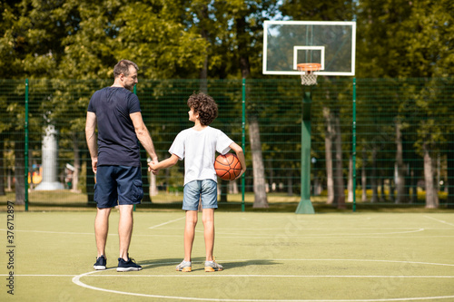 Man posing with little boy on basketball pitch back view