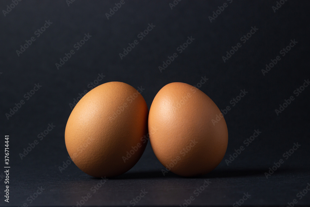 Eggs on a black background. Two chicken eggs next to each other. Eggs on a black background. Two chicken eggs next to each other.