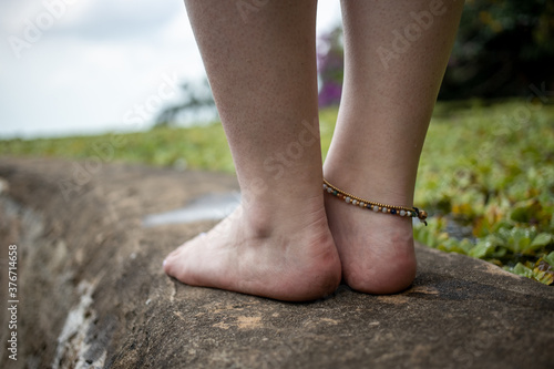 female legs with a bracelet on the side of the pond against the backdrop of a natural landscape