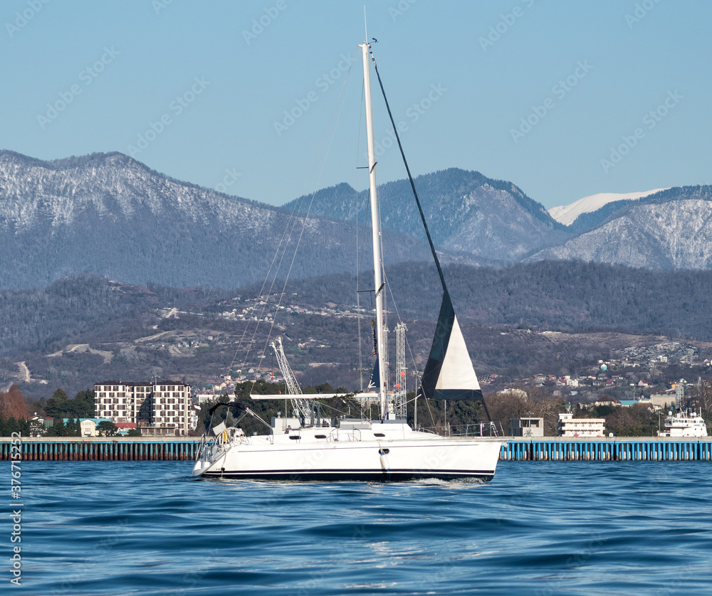 Sailing yacht on sea water at coast and mountains background