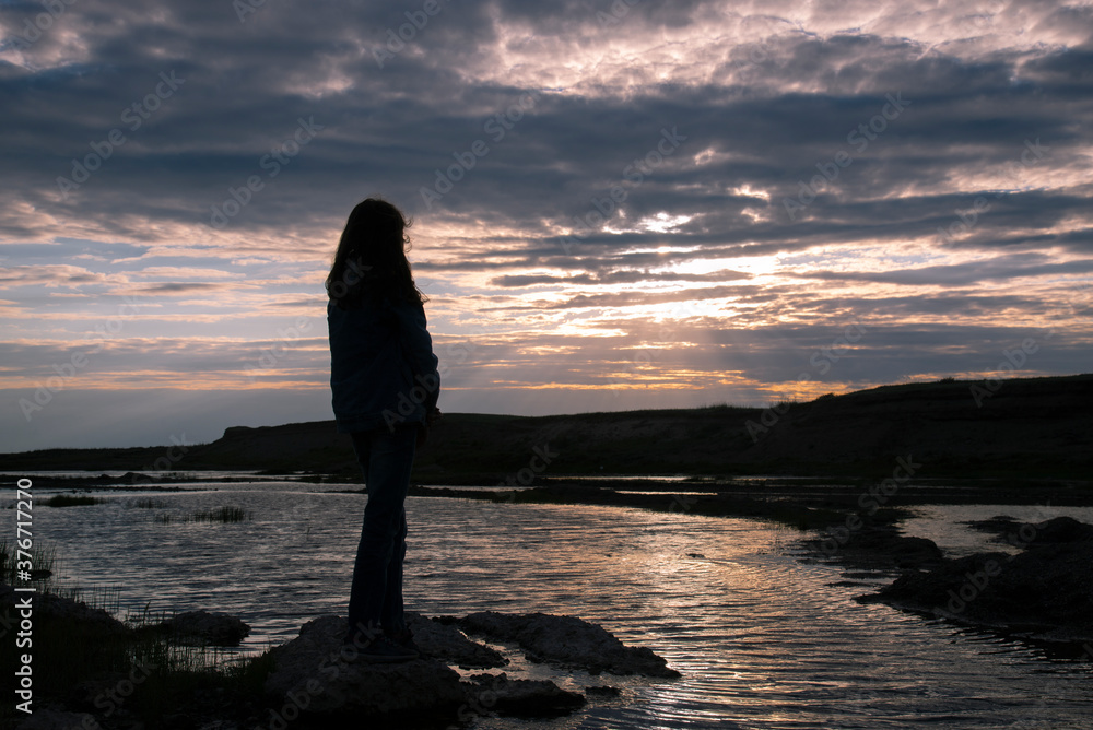 Dark silhouette of a girl with long hair on the river Bank at sunset
